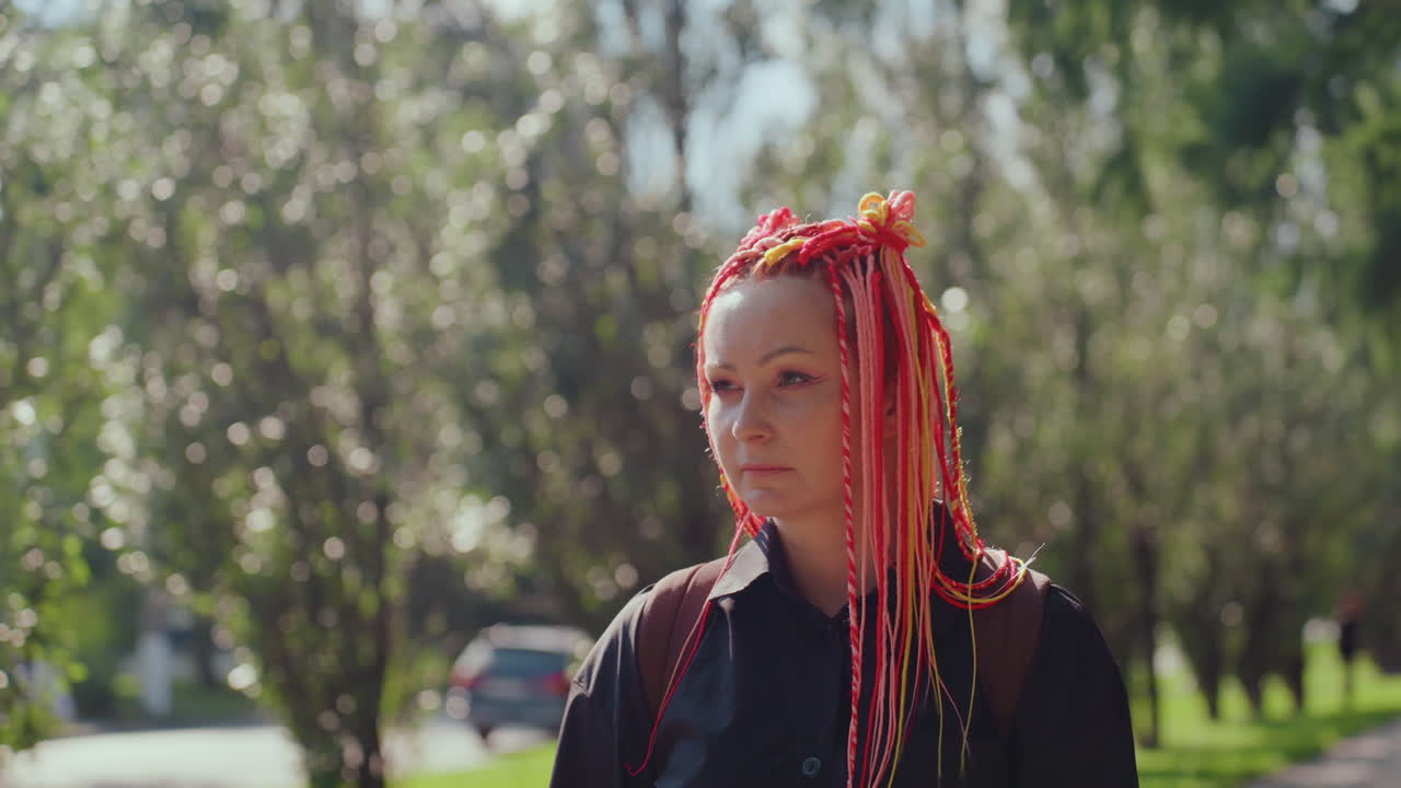 Mujer serena con trenzas rosas al aire libre, mujer caucásica equilibrada mirando con confianza entre árboles iluminados por el sol, mujer tranquila y segura con trenzas rosas de pie en un camino luminoso y sombreado del bosque