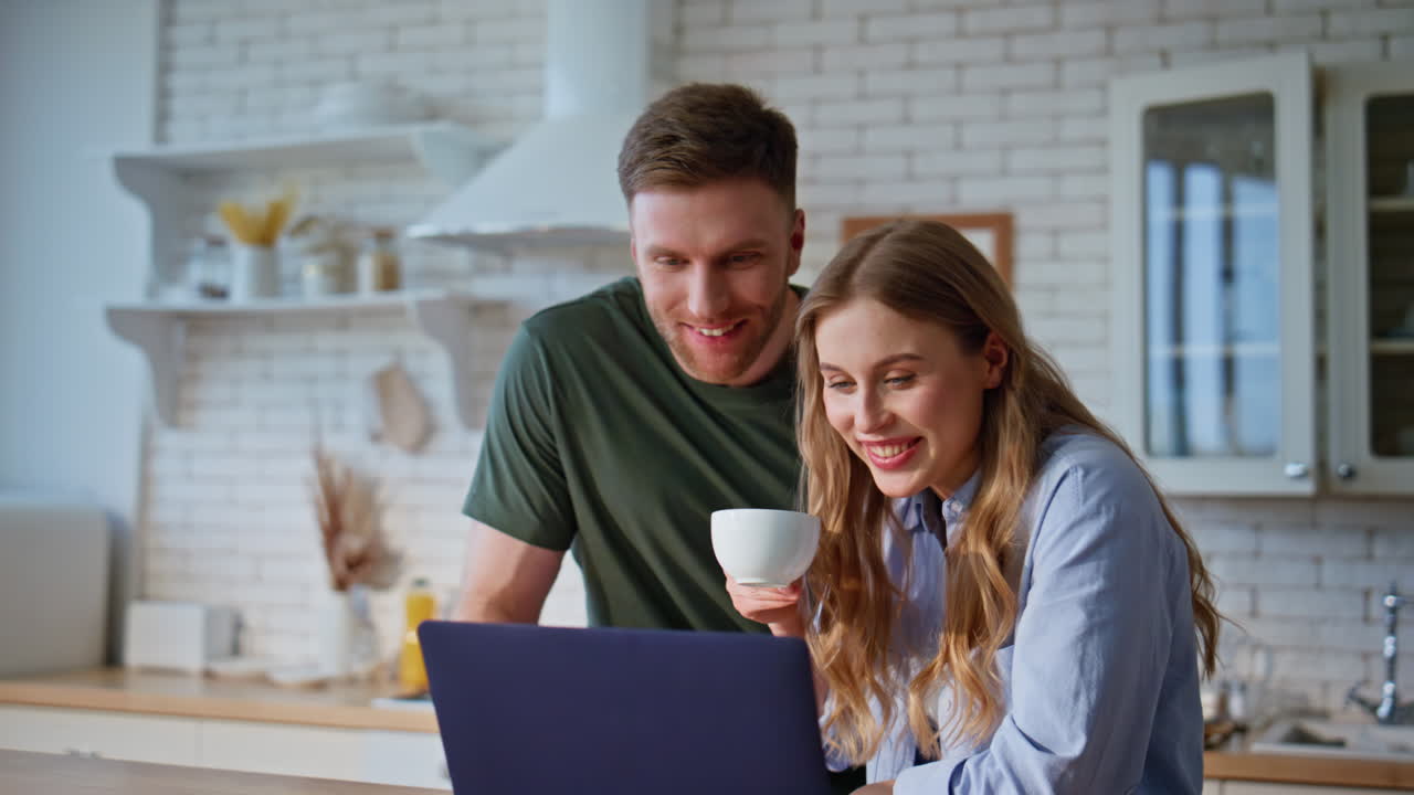 Laughing pair looking computer at family morning closeup. Couple drinking coffee
