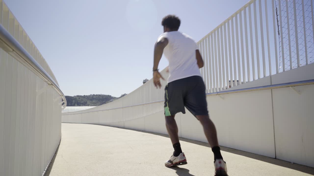 Vista posteriore di un uomo afroamericano sportivo che corre su un ponte