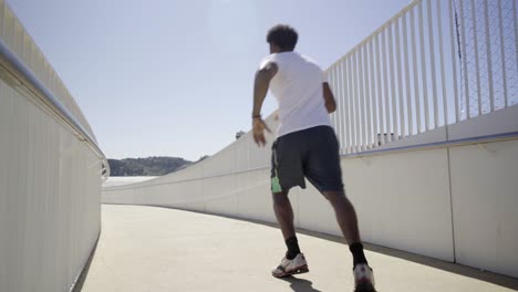 rear view of sporty african american man running on bridge.