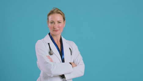 retrato de una doctora con abrigo blanco de pie frente al fondo azul del estudio