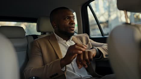 Close-up-a-man-with-Black-skin-and-a-beard-in-a-brown-suit-and-white-shirt-rides-in-a-modern-car-in-the-salon-and-looks-out-the-window