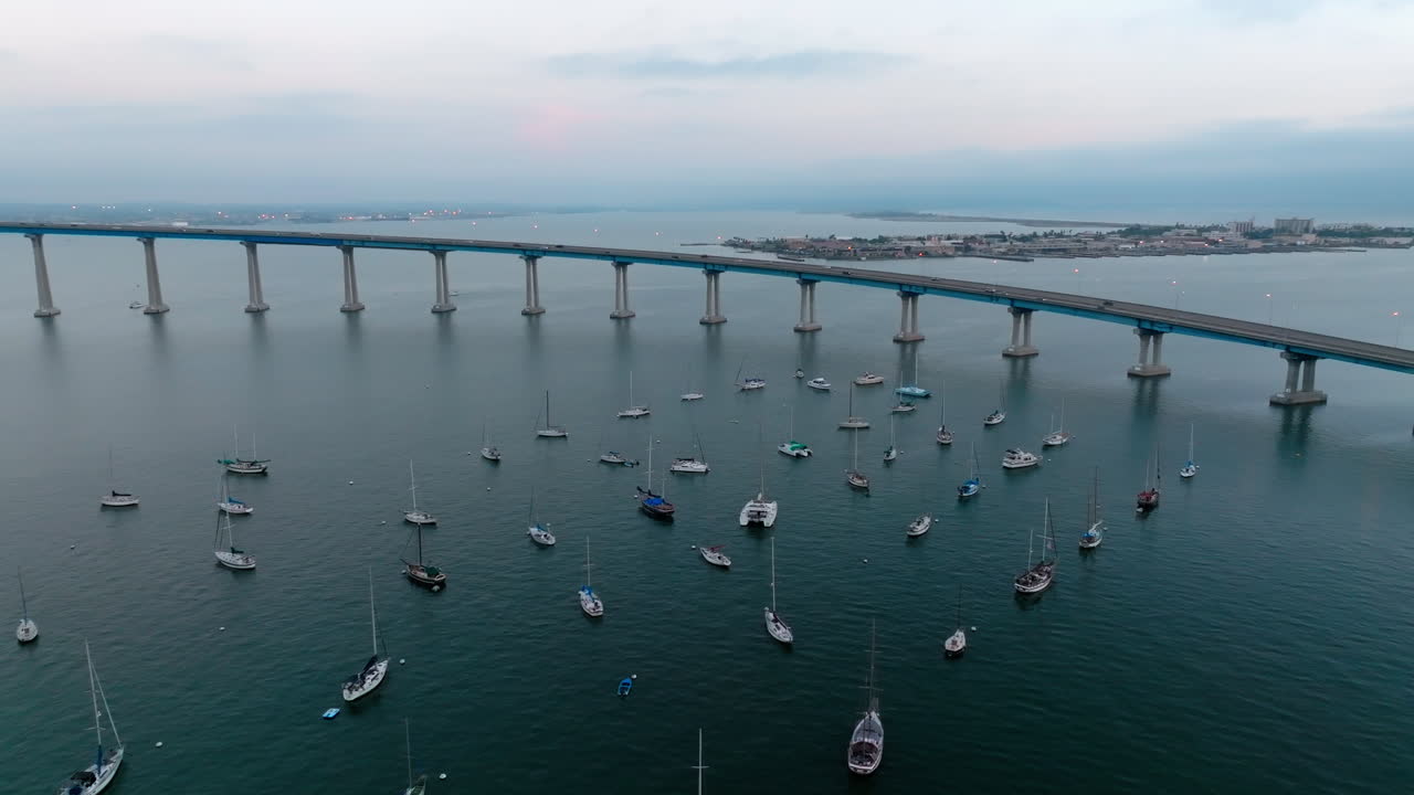 캘리포니아주 샌디에고의 곡선형 코로나도 다리 근처에 주차된 작은 요트와 범선의 영화 같은 드론 샷