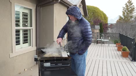 man finishes cooking camp eggs and hash on his flat top griddle and puts them on a pan to serve