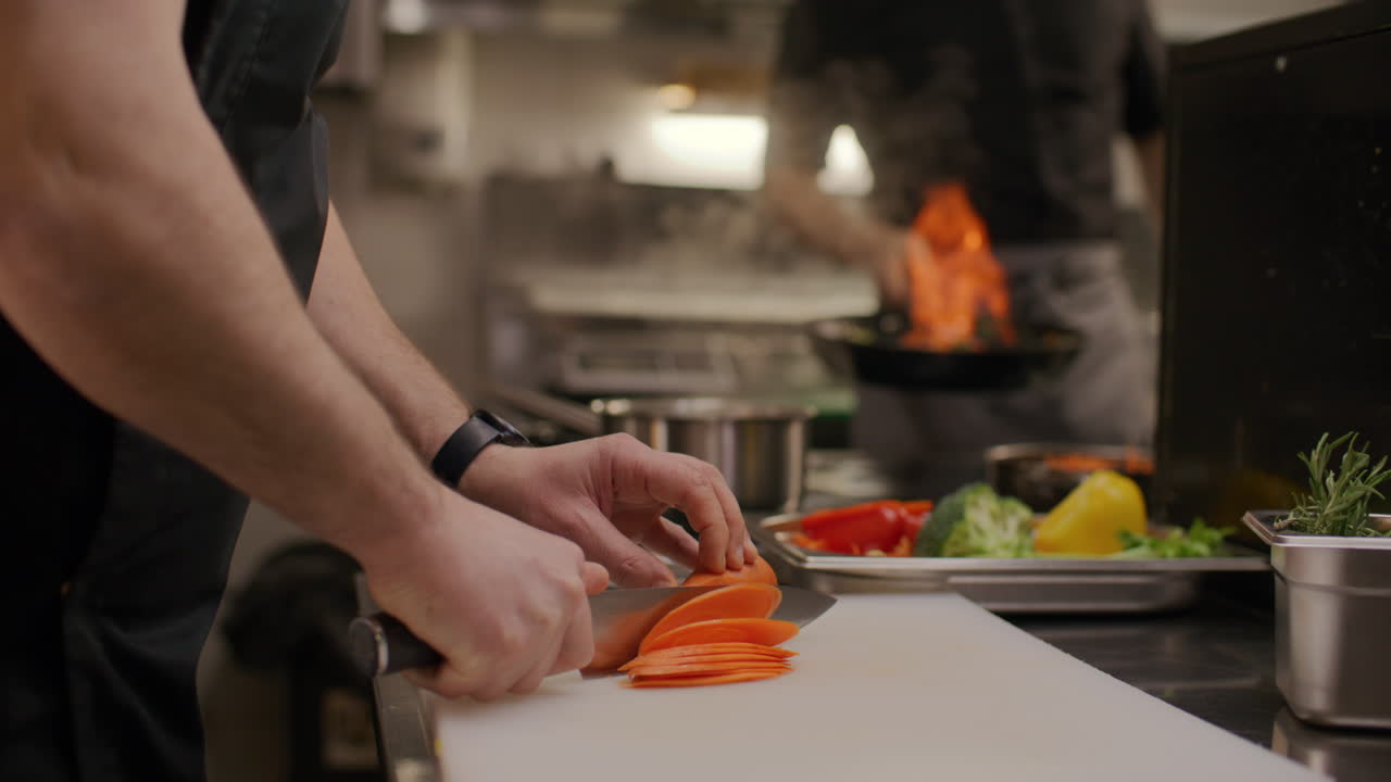 Nærbillede af kok, der skærer gulerod på skærebræt i restaurantkøkken.