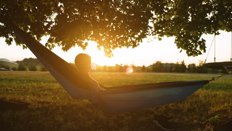 woman relaxes in a hammock at golden hour, looking out over the sunset