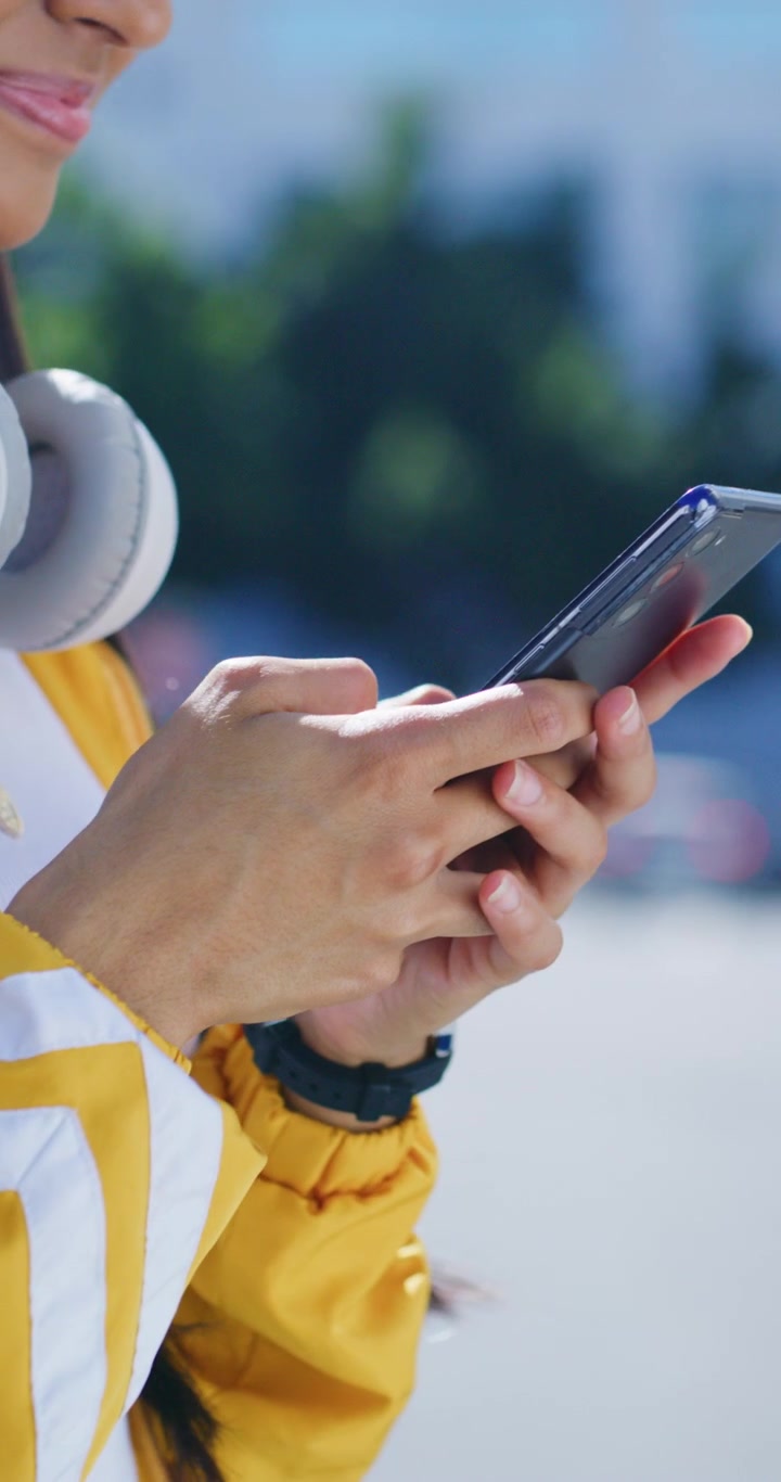 Giovane donna che usa lo smartphone all'aperto con le cuffie intorno al collo