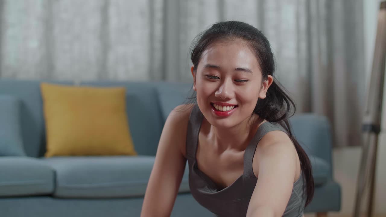 운동복을 입은 젊은 아시아 운동선수 여성이 요가 매트에 앉아서 집에서 햄스트링 스트레칭을 하고 있습니다.