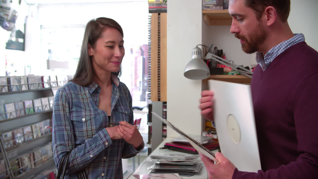 una mujer joven pagando a un hombre en el mostrador de una tienda de discos