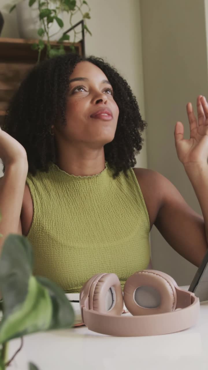 Vertical video: Sitting woman clasping hands and listening at desk near window, pink headphones