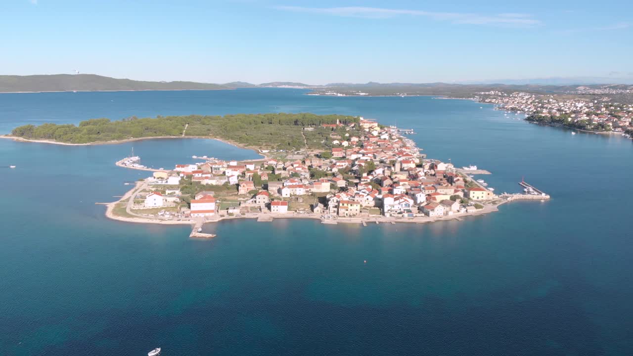 Přelet dronem nad malým ostrovem Krapanj ve Středozemním moři v Chorvatsku, s malým městem za oblačného letního dne, turistická destinace.