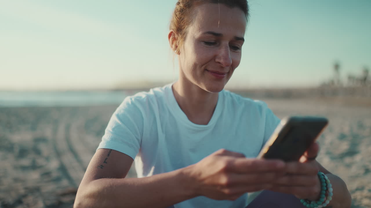 Sportswoman sitting using her smartphone on the beach.