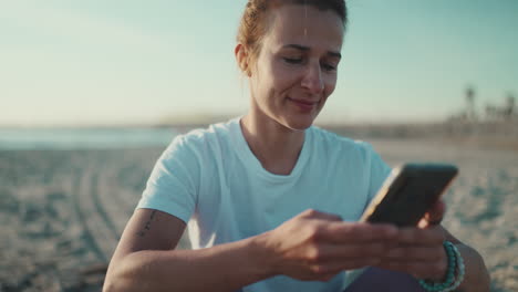 una deportista sentada usando su teléfono inteligente en la playa.
