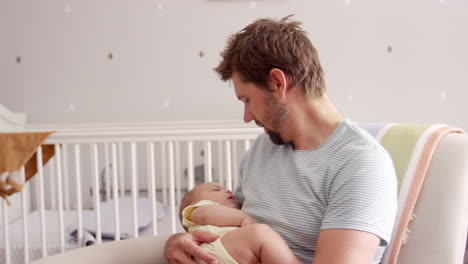 Padre-Sentado-En-Una-Silla-De-Guardería-Sostiene-A-Su-Hijo-Dormido