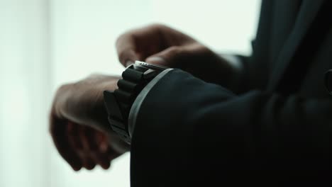 confident businessman in classic blue suit wearing or adjust watch with necktie near window in hotel room. handsome man wearing a nice suit on wedding day.