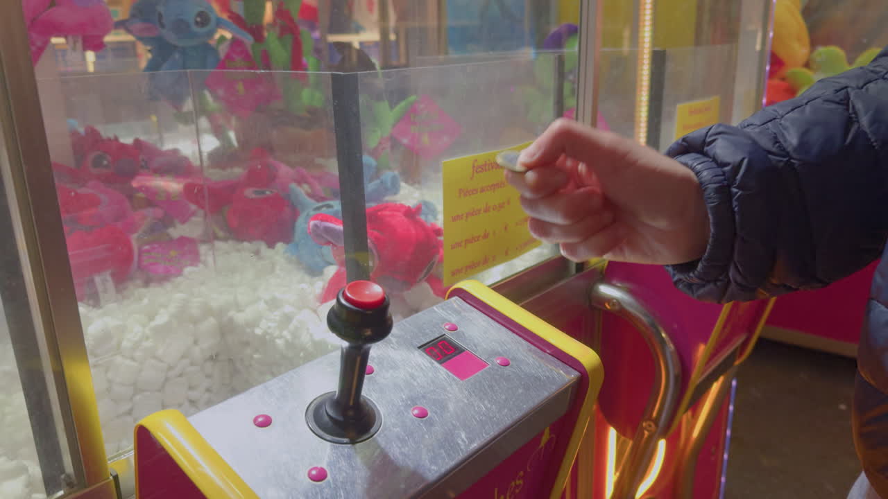 Hand of a man with a coin wishing to play plush machines at small local funfair at night in the city of Montrichard Val de Cher, in France.