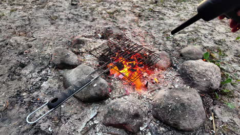 Using-blowtorch-to-ignite-coal,-camping-fire-used-for-cooking-outdoors-in-nature