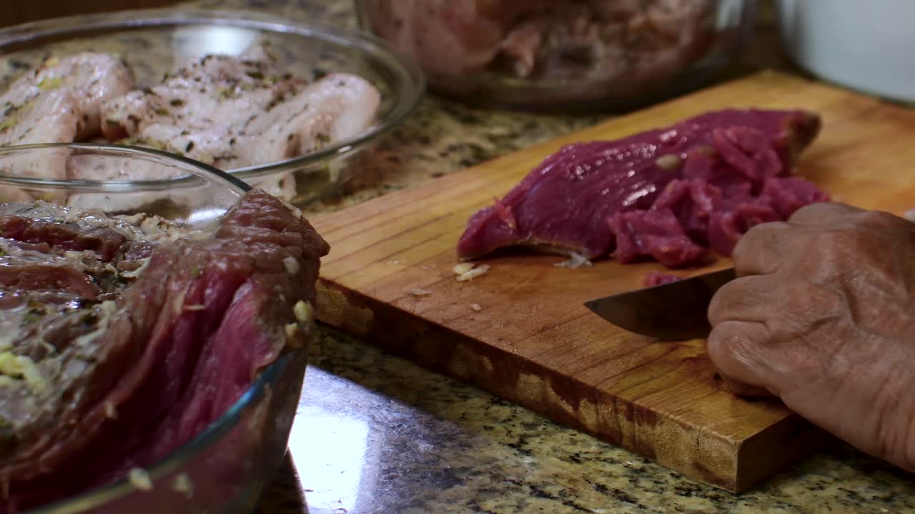 Close-up tangan wanita tua mengiris daging mentah segar di atas talenan di dapur rumah. Persiapan makanan rumahan tradisional
