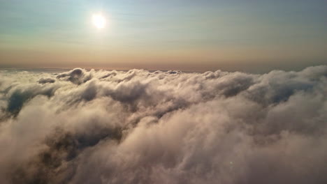 revealing a breathtaking view above a sea of clouds with the sun glowing brightly in the hazy sky, creating a heavenly, ethereal scene - cinematic drone shot pull back reveal