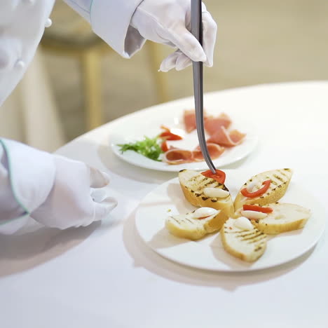 professional cook decorates toasts with slices of meat, tomatoes by kitchen pinchers. beautiful presentation of tasty toasts on a white plate for guests
