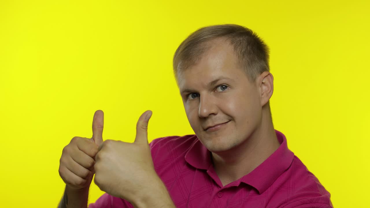 티셔츠를 입고 포즈를 취한 백인 남자의 초상화. 미소 짓는 잘생긴 남자가 엄지손가락을 보여준다. 사람들의 감정