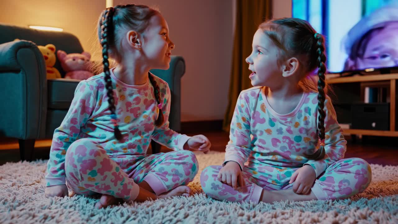 Two Happy Twin Girls in Pajamas Watching TV