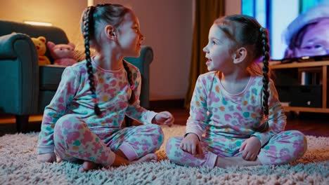 two happy twin girls in pajamas watching tv