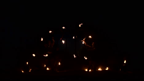 Three-women-with-burning-hoops-dance-with-fiery-torches-in-leather-clothes-in-a-dark-hangar-demonstrating-a-circus-fire-show-in-slow-motion