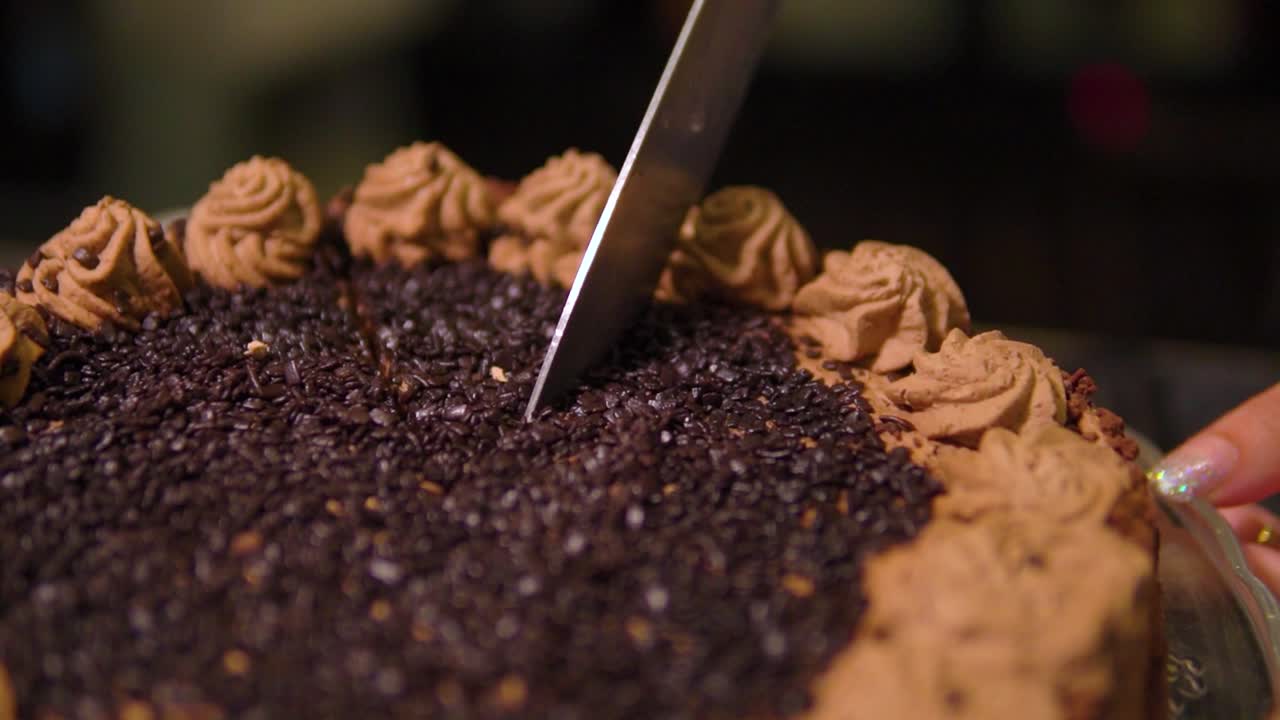 Cutting a delicious chocolate cake with brown cream on top into a pieces in restaurant slow motion