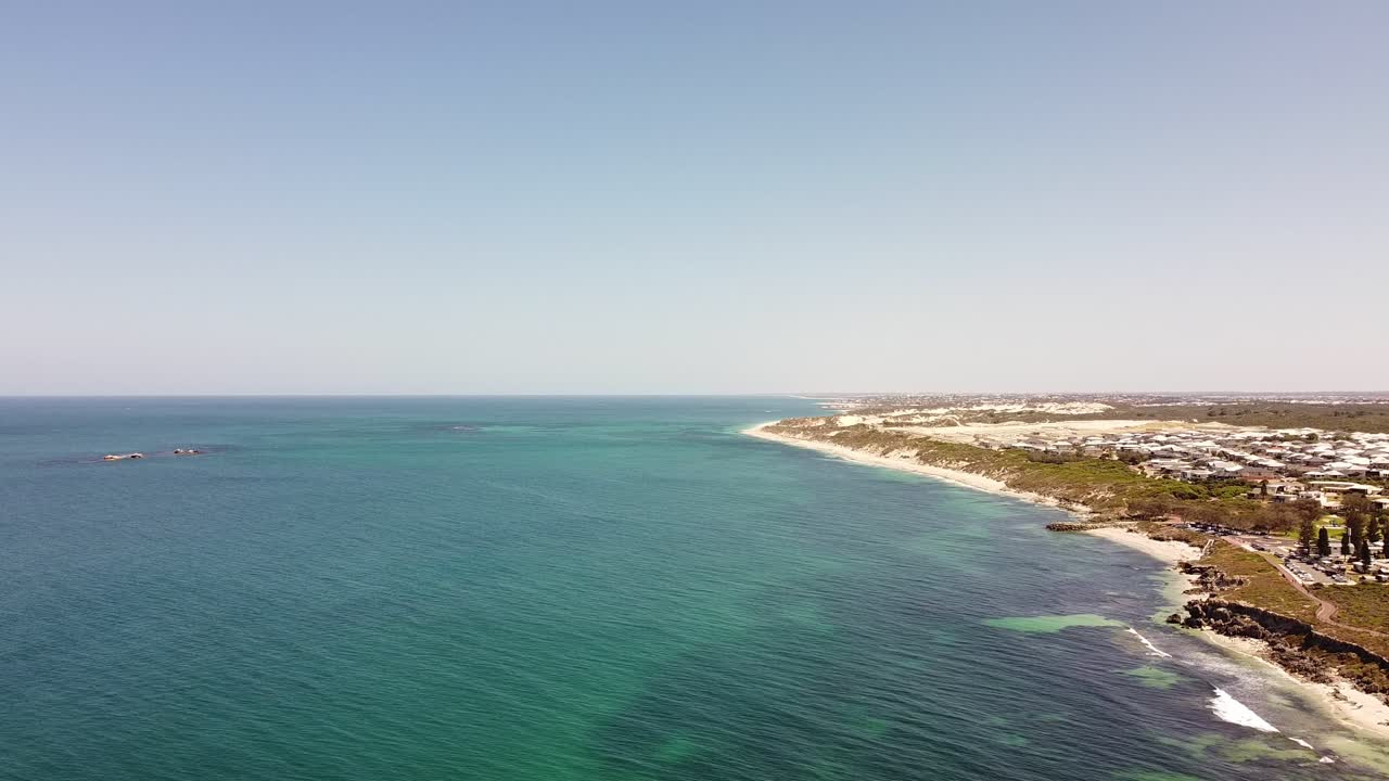 Acqua di mare blu, spiaggia di sabbia bianca e vegetazione verde, ripresa aerea statica.