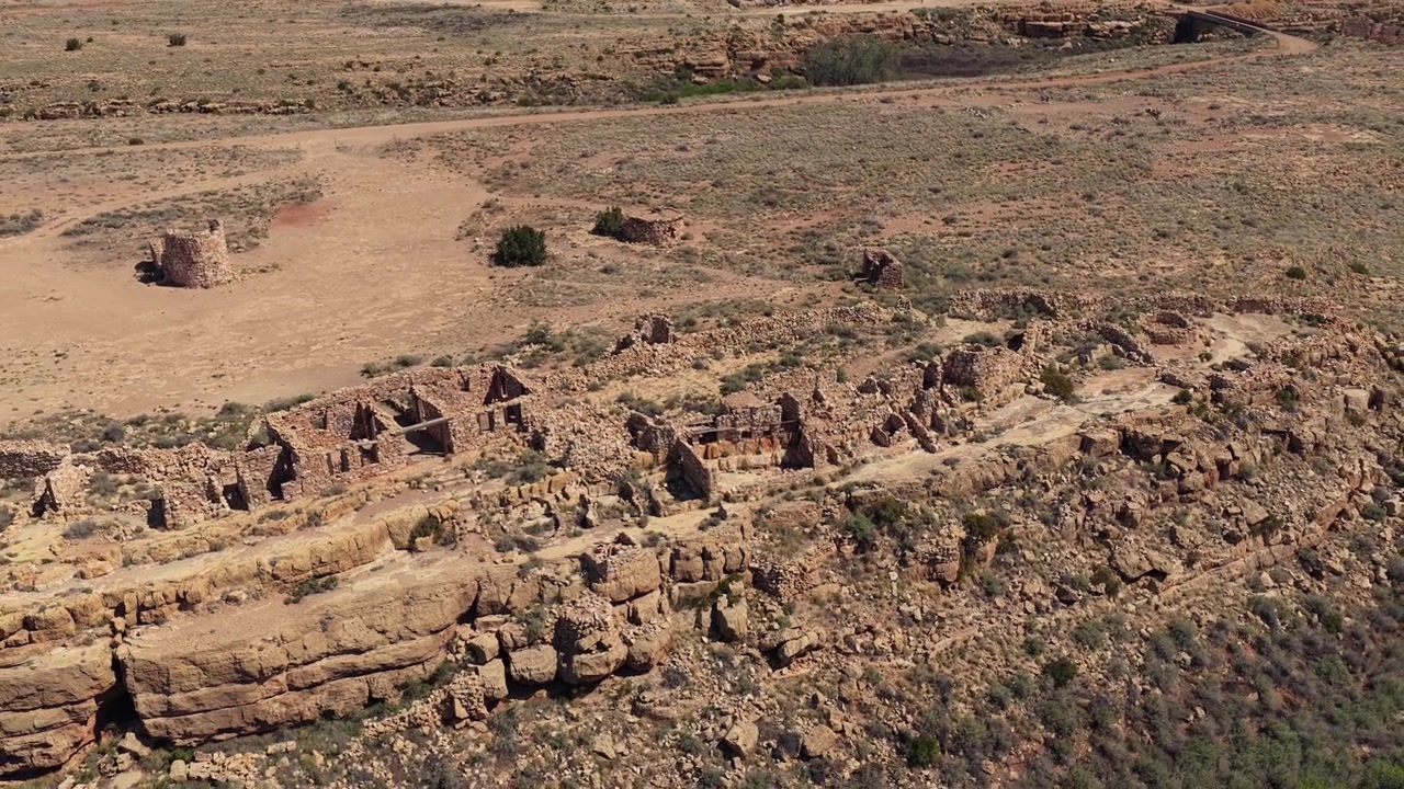 A cinematic drone view explores abandoned stone ruins from the cowboy era. These historical structures sit on the edge of a rugged southwest desert canyon, showcasing the decay of the Old West.