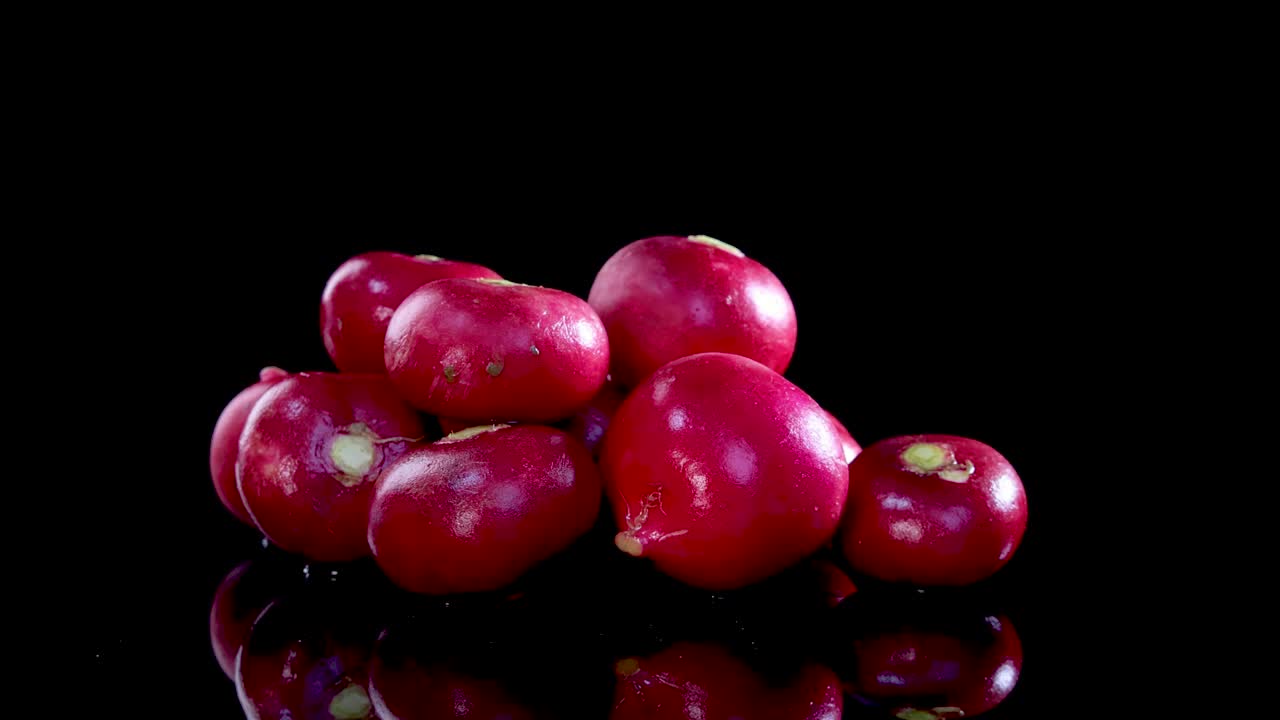 A pile of radishes rotates on a glossy black surface, highlighting their vibrant color and smooth texture