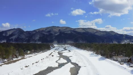 the drone gracefully glides above a river in the winter landscape of hakuba valley in japan, capturing an aerial view that showcases the beauty of the frozen waterway and the mountains around