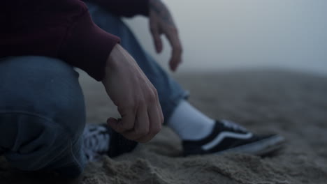 Closeup-unrecognizable-man-sitting-on-beach.-Young-guy-holding-wet-sand-in-hand