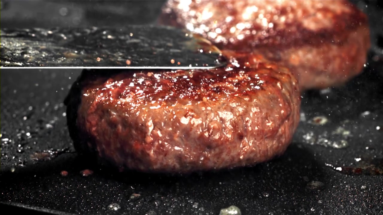 Spatula Pressing a Juicy Hamburger Patty on a Hot Griddle