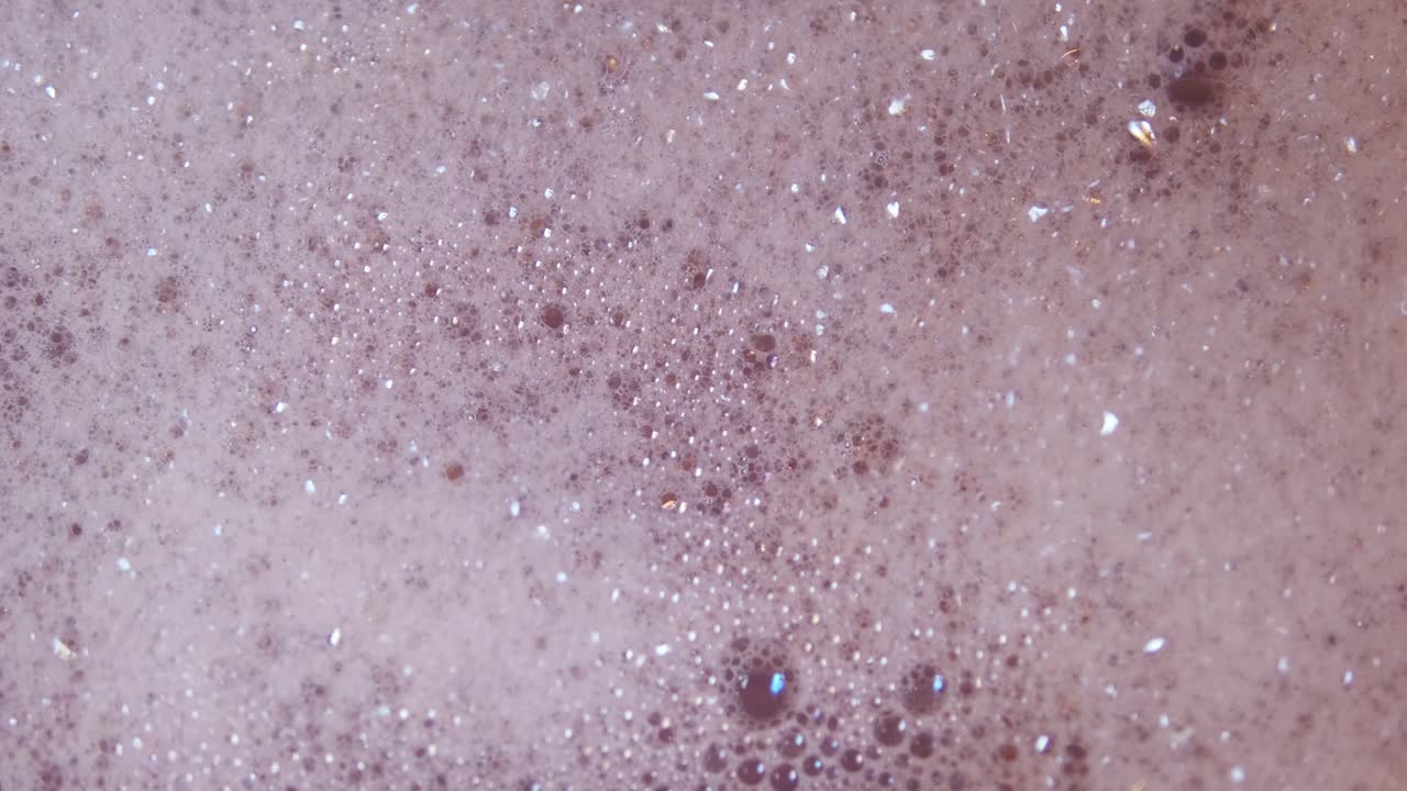 Close up top view of foam and soapy bubbles on a moving water surface, self care, bathtub, pink background