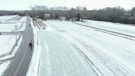 los buggies tirados por caballos conducen por una carretera rural en un campo cubierto de nieve, un seguimiento aéreo del paisaje rural cubierto de nieve fresca, el condado de lancaster, pa