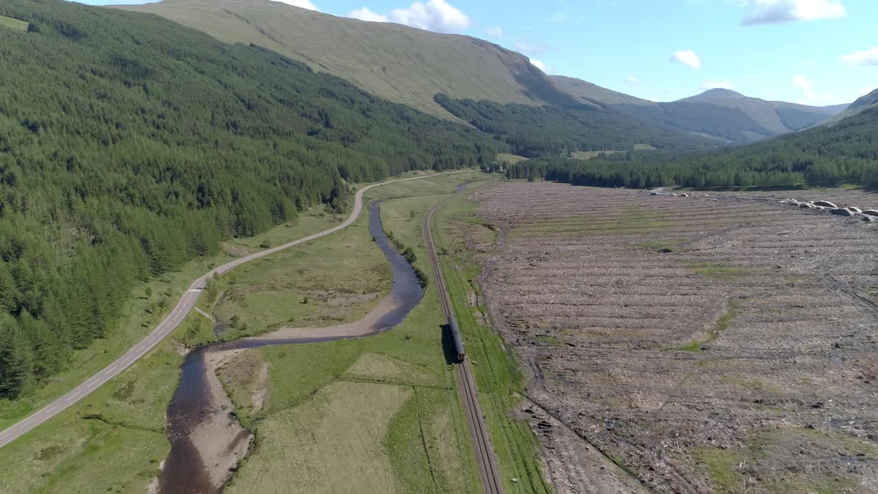 toma aérea de alta extracción a través de glen lochy mientras el tren de cercanías viaja a lo largo de la vía que se dirige a la ciudad de oban