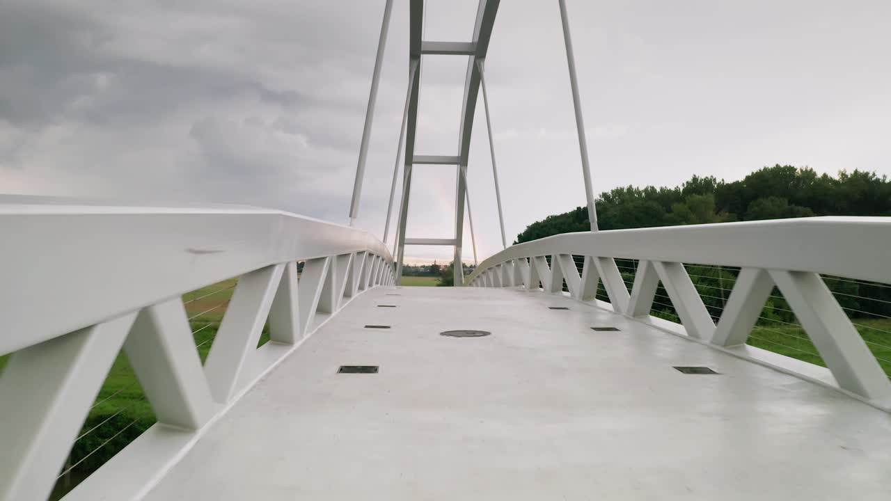 Flying forward through a cycling bridge running across calm river Moravia in Slovakia. Aerial sunset footage taken just before a storm