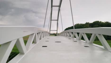 flying forward through a cycling bridge running across calm river moravia in slovakia. aerial sunset footage taken just before a storm
