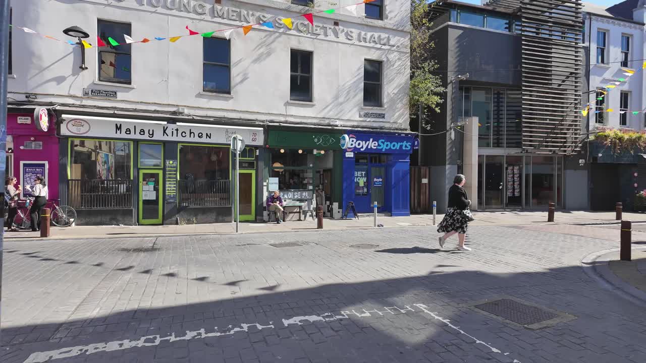 Cork City Main street with festive flags and people, pubs and Boyle bookmakers, sunny Ireland