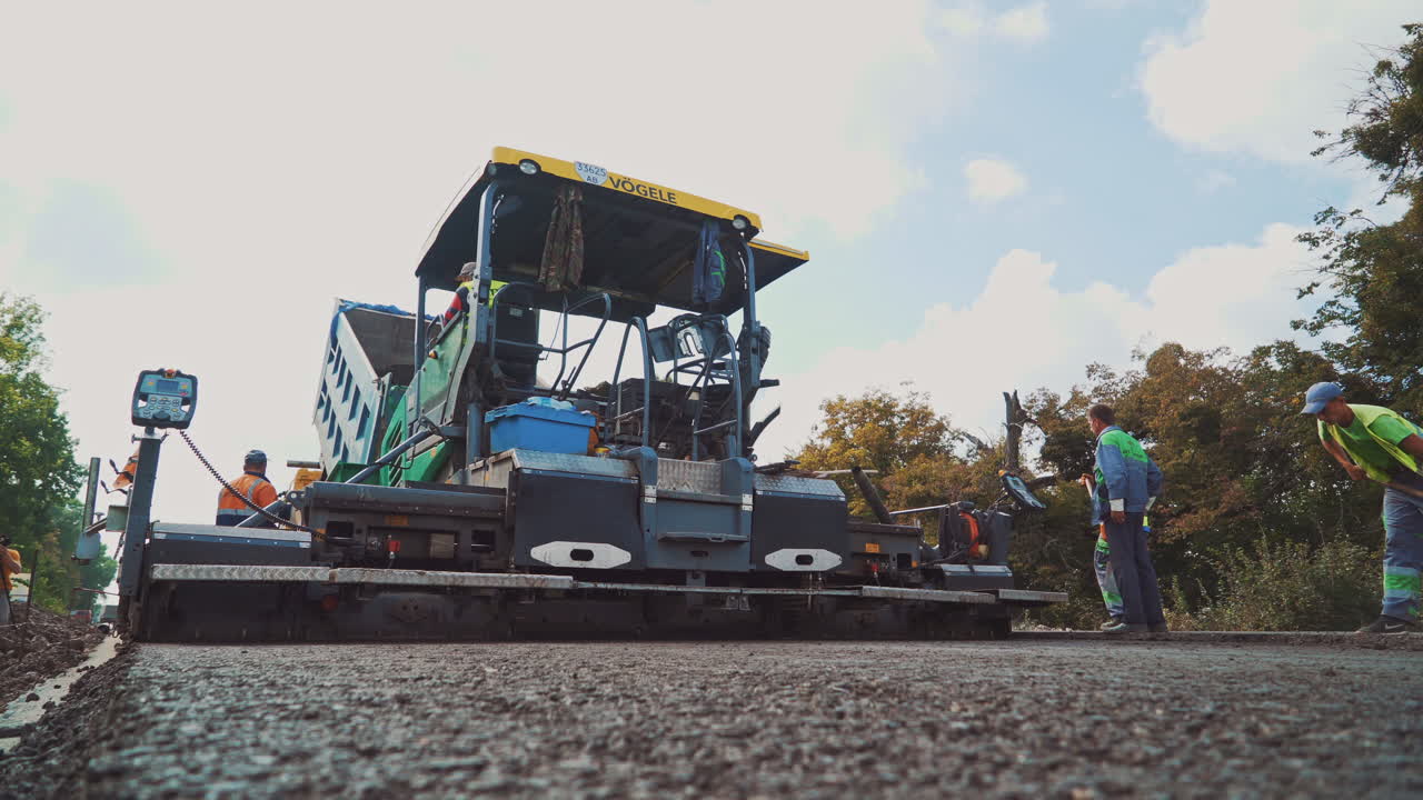 Huge asphalt paver machine and workers. Fresh asphalt is spreading on the road with new technique and a crew of workers.