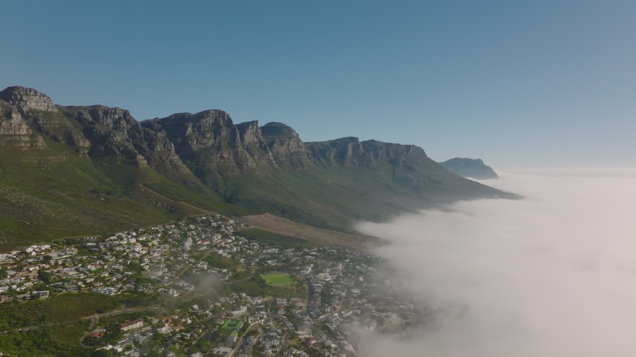 Incredibile filmato aereo panoramico in discesa di una cresta montuosa rocciosa che si erge su un paesaggio inondato dalla nebbia costiera. Città del Capo, Sudafrica