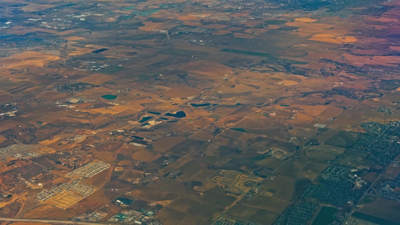 Patchwork farmland and rural development stretching across expansive plains, aerial with sunlit patches