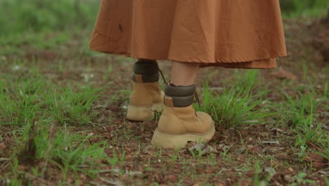 person wearing boots and a long skirt walks on a grassy path