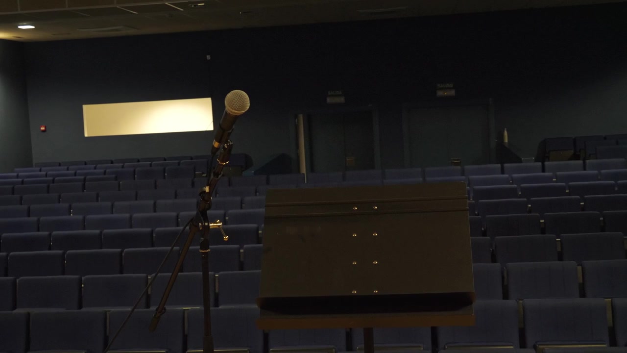 Ripresa POV del palco con un'asta per microfono e un leggio di fronte a file di sedili vuoti in un auditorium buio. Concetto per paura del palcoscenico, preparazione di eventi o teatro vuoto.