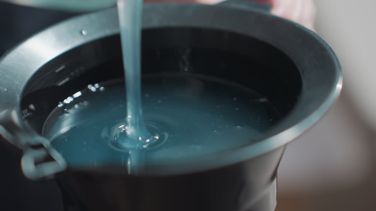 파란색 염색약을 젓는 백인 여성의 손, 혼합 용기를 안정적으로 잡고 있는 스타일리스트의 손, 스포이트에서 흘러나오는 점성 있는 색상, 집중된 기술이 돋보이는 미용실 준비 장면, 윤기 있는 마무리, 직접 체험