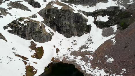 Toma-Aérea-Inclinada-Mirando-Desde-Un-Pequeño-Lago-Hasta-Las-Cimas-De-Las-Montañas