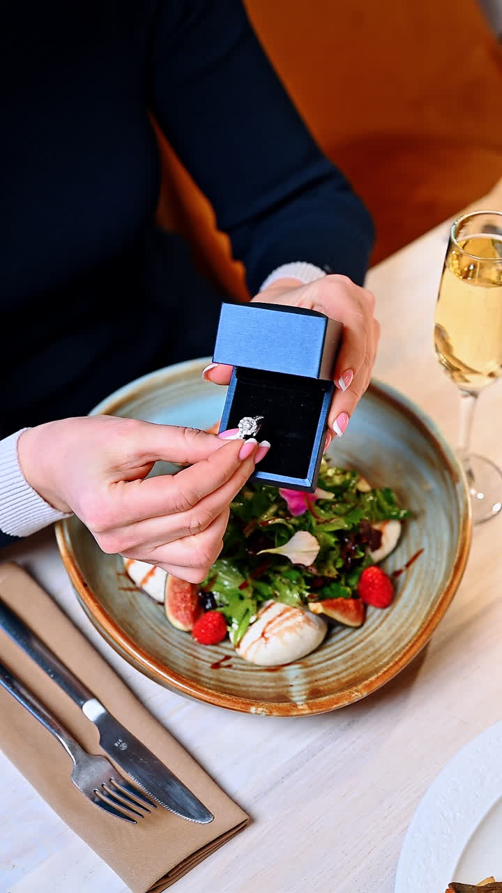 Engagement proposal during dinner at a restaurant with a salad and champagne. Person proposes with a ring while holding a salad in a restaurant setting with a drink