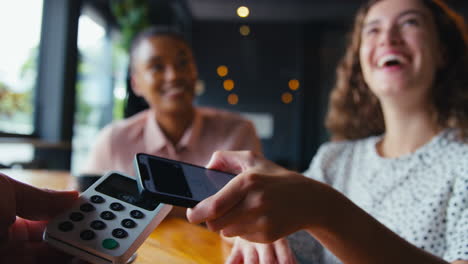 woman in coffee shop paying bill with contactless mobile phone payment